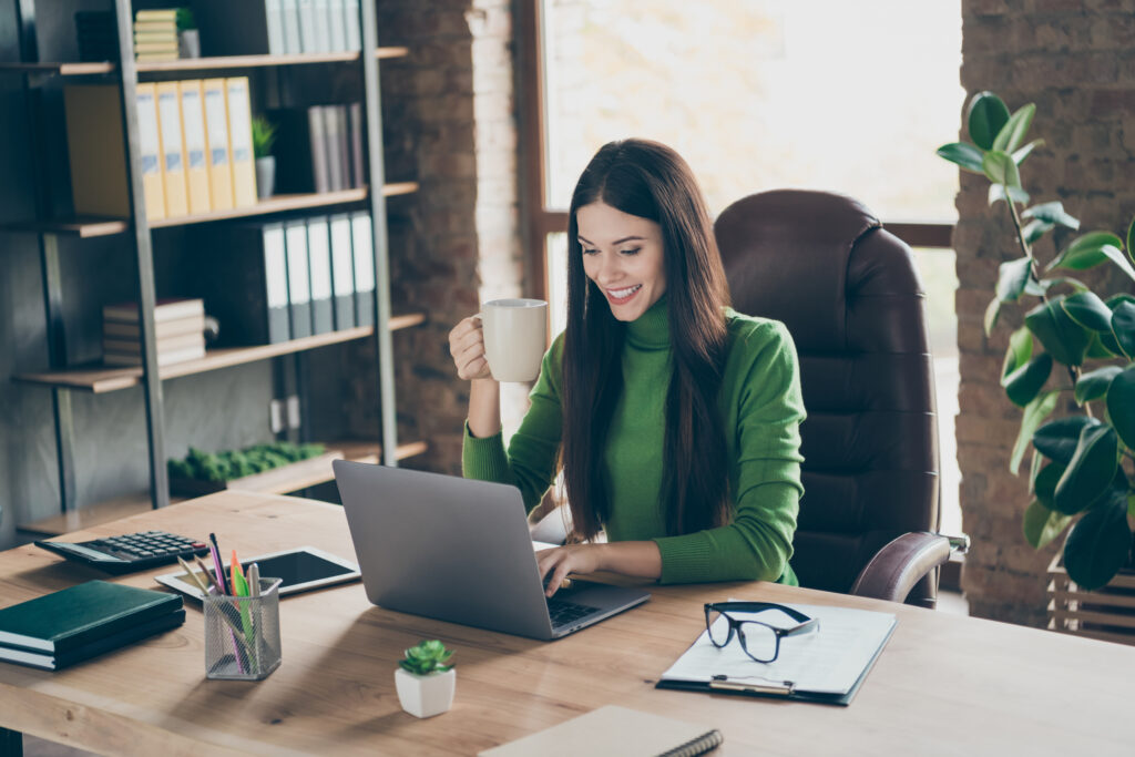 Profile photo of pretty young business lady looking screen notebook table modern user chatting partners drink hot tea mug sitting boss chair wear green turtleneck modern interior office